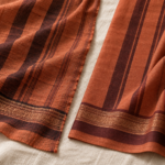 Close-up comparison of a handwoven saree border with a slightly uneven selvedge and natural slubs, next to a machine-woven powerloom fabric with a perfectly straight edge, on a warm cream background